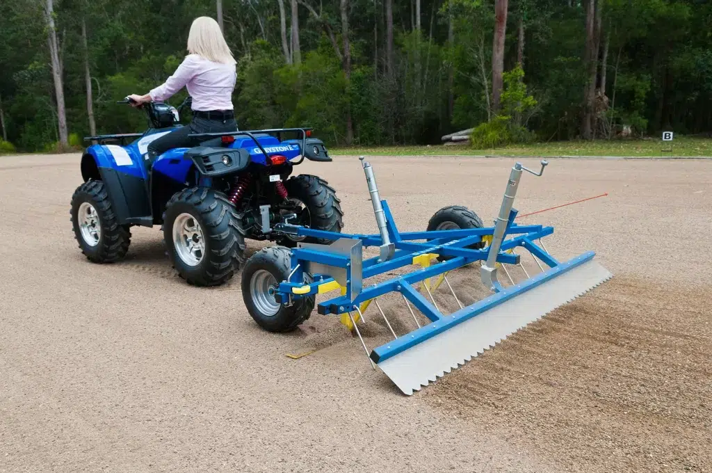 Greystone Arena Rake Pro attached to a small tractor, highlighting its flexibility in towing options and ease of maneuverability